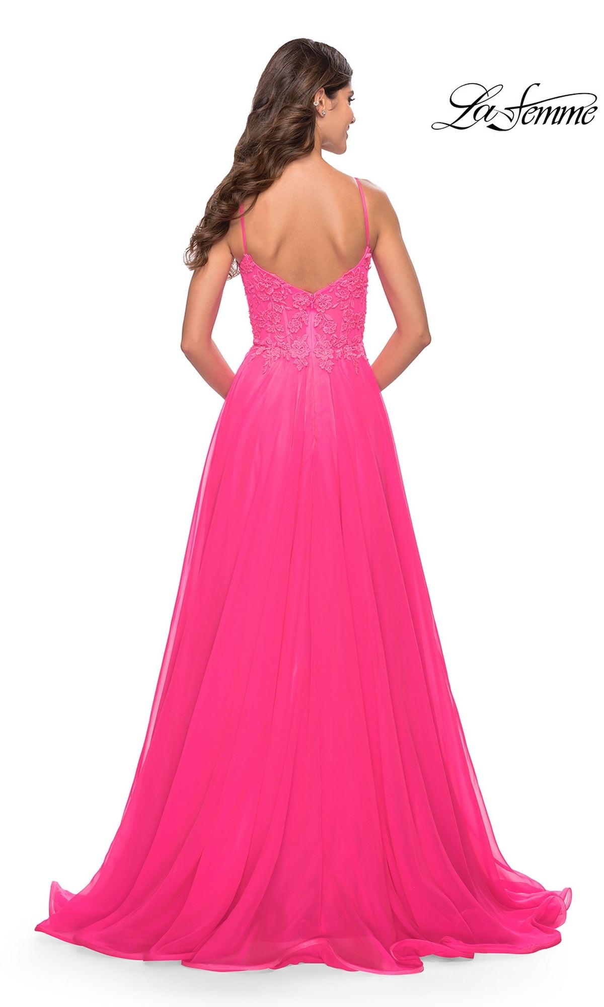 A woman faces away in the La Femme Neon Pink Long A-Line Prom Dress 31506, featuring an embroidered v-neck bodice with thin straps, delicate lace details, and a flowing skirt.